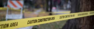 Yellow caution construction area tape stretched across a tree-lined job site