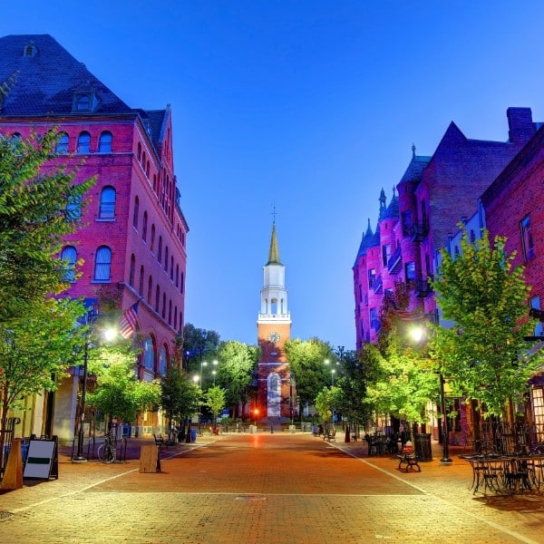 Burlington Church Street at dusk with historic brick buildings and green street trees illuminated by lights